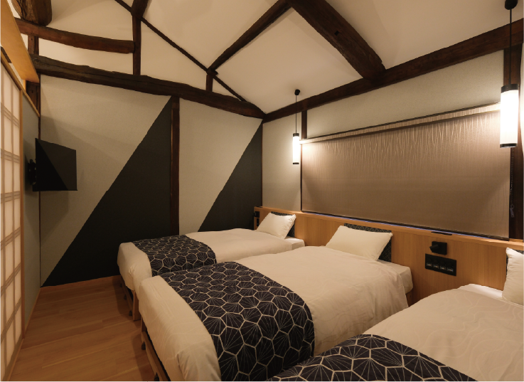 壁に取り付けられたテレビとベッドが3つ並んだ寝室の写真